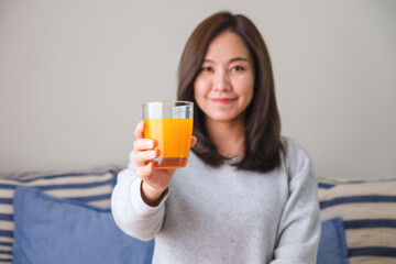 Portrait image of a young woman holding and drinking fresh orange juice at home
