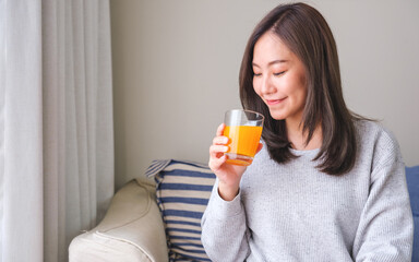 Portrait image of a young woman holding and drinking fresh orange juice at home