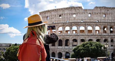 Back view of young woman tourist with hat she's take a picture by smartphone at Colosseum in Rome, Italy.