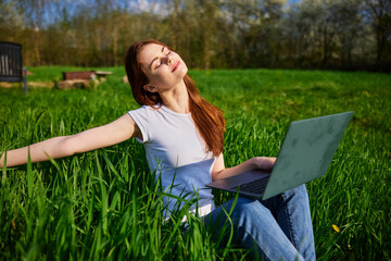 joyful woman works sitting in high grass behind a laptop raising her hand up