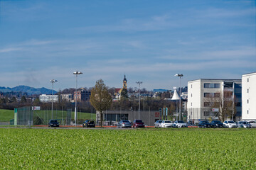Emmenbrücke with church tower and scenic landscape, tennis courts, skyline and Swiss Alps in the background on a sunny spring day. Photo taken March 22nd, 2023, Emmen, Switzerland.