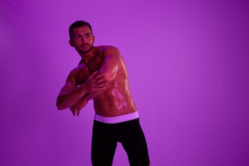 Man athletic body bodybuilder in briefs with nude torso abs full-length in the background fitness classes, purple colored light. Advertising, sports, active lifestyle, competition, challenge concept. 