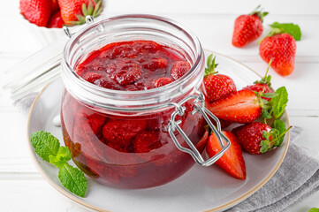 Strawberry jam in the glass jar with fresh berries on a white wooden table. Summer dessert. Copy space.