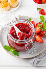 Strawberry jam in the glass jar with fresh berries on a white wooden table. Summer dessert. Copy space.