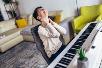 Little boy playing piano in living room. The boy is suffering from neck pain.