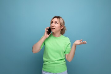doubtful attractive blond girl holding a smartphone in her hand on a blue background with copy space