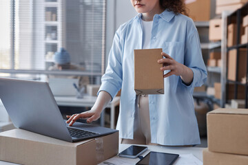 Cropped shot of young female worker of post office checking address of receiver on top of packed...