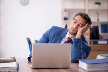 Fototapeta premium Young male employee unhappy with excessive work in the office