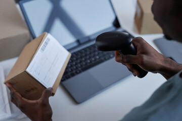 Hand of young African American male worker of post office scanning code on box while checking...