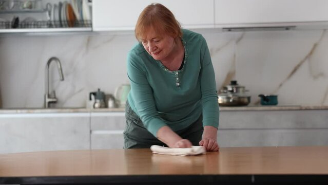 Happy mature woman cleaning her kitchen with radiant smile . High quality 4k footage