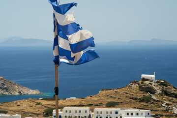 View of the greek national flag waving in the wind at the top of the village of Ios in Greece and...