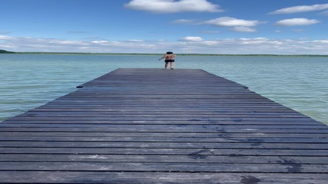 Boy run on wooden dais and jump in water, vertical video. Happy kid diving in sea. Active lifestyle, marine tourism.