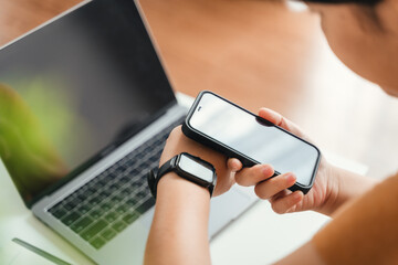 .Woman use smartphone and smartwatch for tracking activity on sofa in living room at home, wireless connection between the watch and mobile phone.