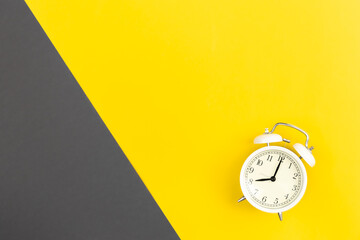 White alarm clock on a yellow and green background, flat lay.