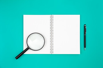 Blank notepad, magnifier and pen on a blue background, flat lay.