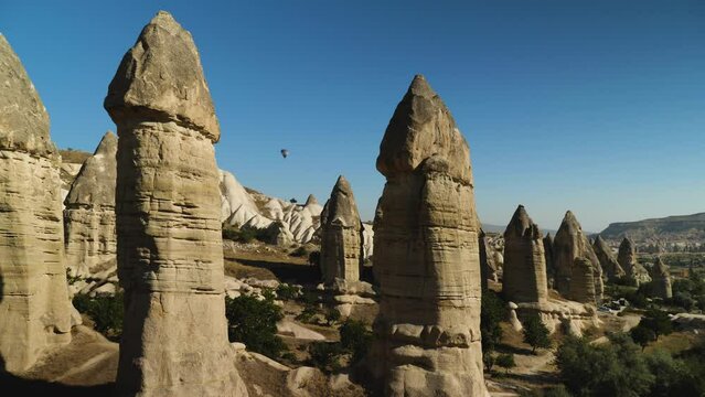 Close-up of sandstone cliffs in the form of phalos. Valley of Love in Cappadocia. Against the backdrop of a blue sky with balloons. Camera movement from left to right