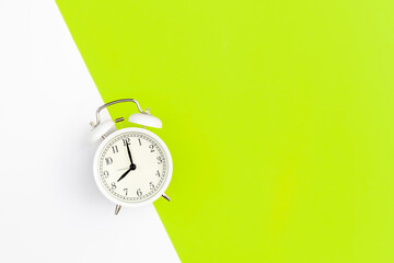 White alarm clock on a white and green background, flat lay.