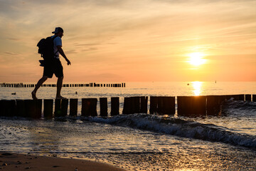 Mann balanciert auf Buhnen am Strand im Sonnenuntergang an der Ostsee