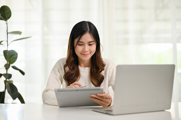 Happy Asian woman using her digital tablet at a table in her home office.