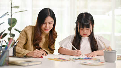 Obraz premium Attractive Asian sister helping her little sister to draw and paint with oil pastel color