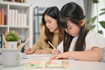 Cute young Asian girl drawing cute animals on paper, spending creativity time with her mother