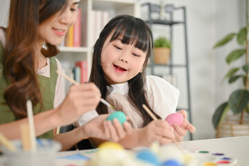 An adorable little Asian girl enjoys coloring Easter eggs with her mother