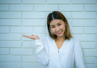 Beautiful asian business woman standing with a smile while looking to the camera against a white brick background, Digital marketing.