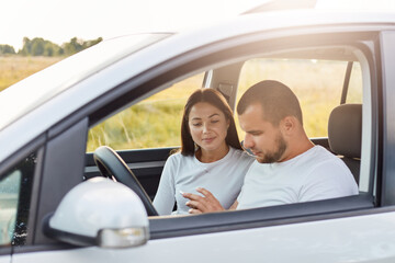 Portrait of young couple in new car traveling, using cell phone navigator to know right way, man holding mobile phone in hands, family having journey.