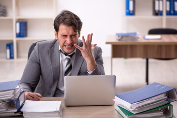 Fototapeta premium Young male employee unhappy with excessive work in the office