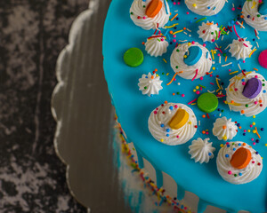 Very colorful cake decorated with blue icing on a cement table.