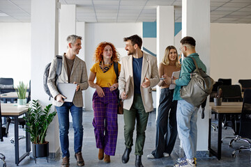 Coworkers talking while walking through corridor at office 