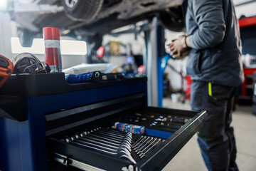 Selective focus on wrenches and tools at the mechanic's workshop with worker repairing the car in...