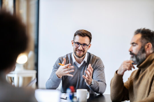 A businessman is sitting in boardroom with team and explaining his ideas.