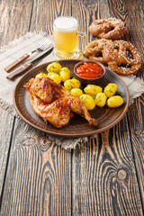 Bavarian roast chicken Hendl with boiled potatoes served with beer and pretzel closeup on the wooden table. Vertical