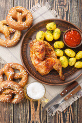 Oktoberfest Roast Chicken Wiesn Hendl with potatoes served with beer and pretzel closeup on the wooden table. Vertical top view from above