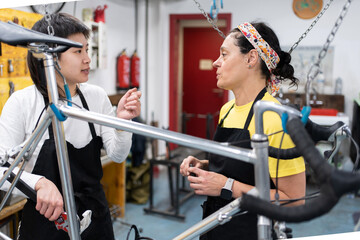 Asian girl asking woman in her forties about bike maintenance in self-repair workshop, bicycle hanging and girls in black aprons.