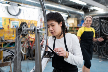 young asian woman in collective self-repair workshop alienating bicycle wheel with tool. Dressed in...