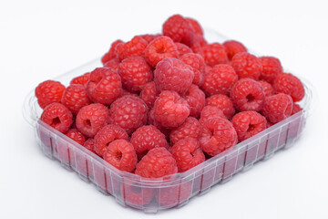 Obraz premium Czerwone, dojrzałe, owoce malin w plastikowym pojemniku na białym tle