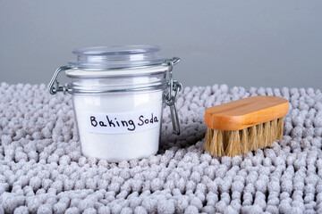 Baking soda and wooden cleaning brush on a gray carpet at home. The concept ecological cleaning and...