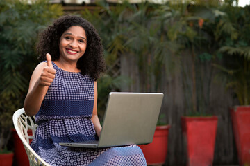 Indian woman sitting outdoor and using laptop and showing thumps up
