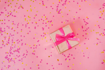 Gift box tied with a pink bow for birthday, mom's day or Valentine's day on a pink background with confetti