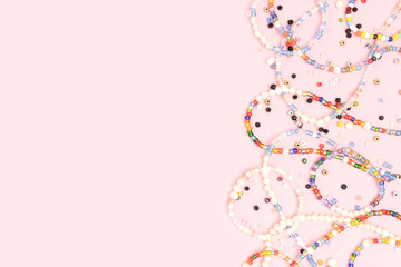Necklaces and bracelets made from beads and pearls scattered on a pink background with copyspace.