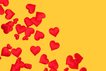 Red textile hearts confetti scattered on a yellow background. Place for text.