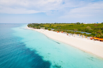 Fototapeta premium The aerial view of Zanzibar's beaches captures the essence of a tropical paradise with palm trees, umbrellas, white sand, and the sparkling blue waters of the Indian Ocean.