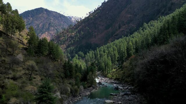 drone shot - flying over the Parvati river in Parvati valley, a beautiful mountain landscape with a river and a snow mountain at the background - Kasol -  Himachal Pradesh, Himalayas -  Northern India