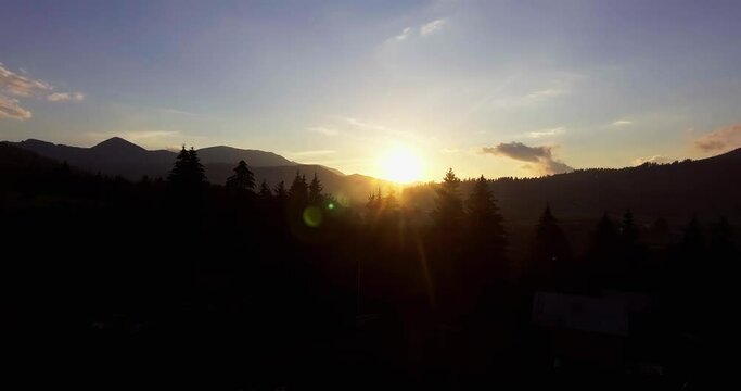 sunset in the mountains. the sun hides behind the mountains and the forest. backlight drone view bright fiery sun.