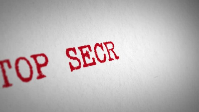 Manual typewriter types the words &lsquo;Top Secret - Classified&rsquo; in red ink onto textured white paper