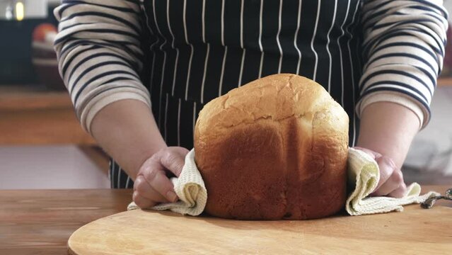 The woman takes homemade bread out of the mold and puts it on the table in a towel