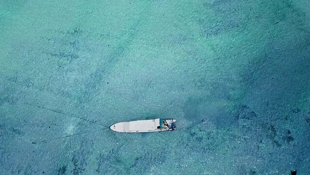 Idyllic aerial of white boat swimming in shallow blue ocean in Nusa Lembongan, Selat Ceningan, Bali. Beautiful shimmering crystal clear water. Drone top down bird's eye view flying forward. 4K