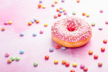 Donut with icing and chocolate chips on pastel pink background